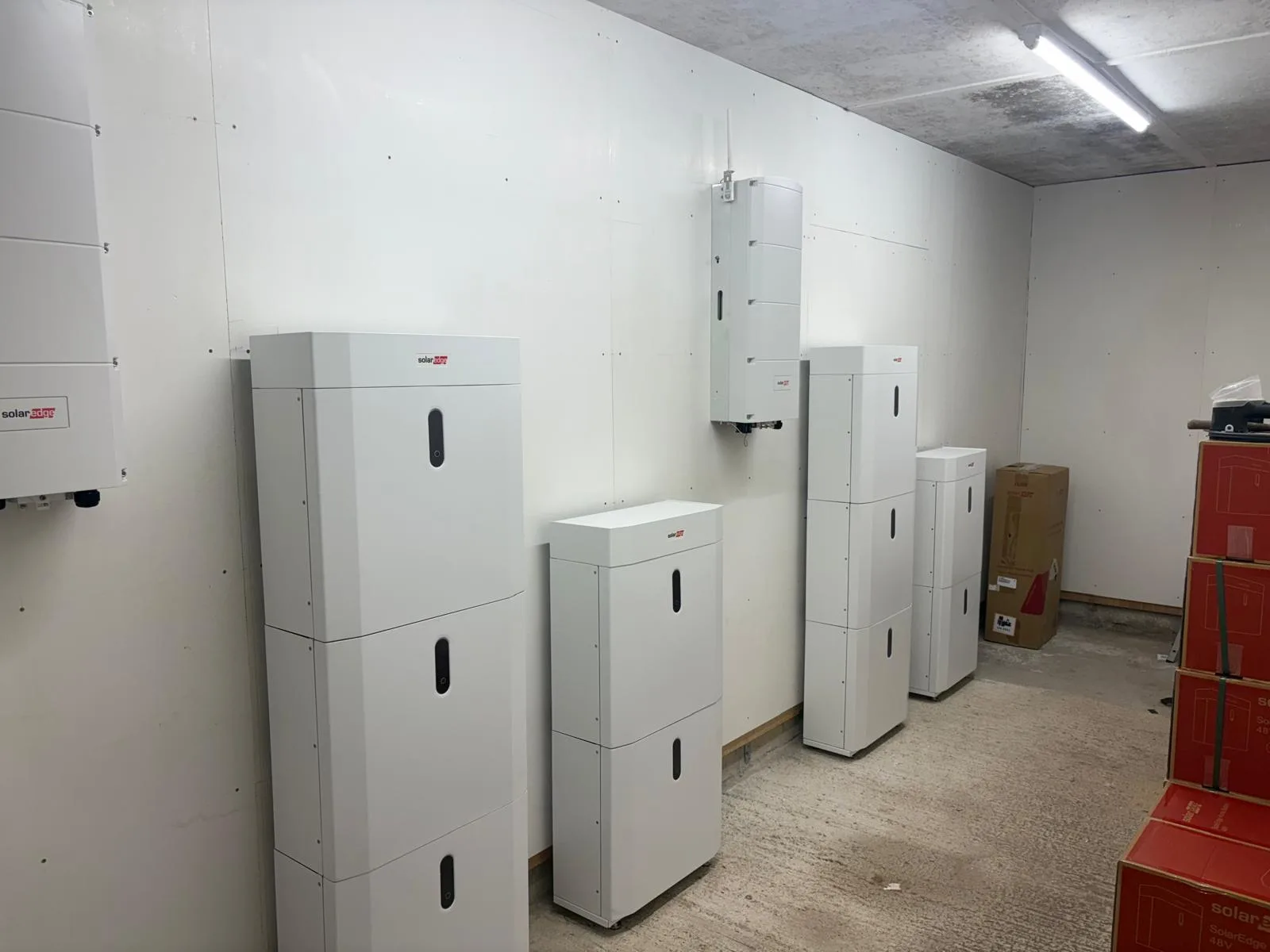 Rows of white floor-standing and wall-mounted electrical storage units in a white room, with red equipment cases stacked at the right.
