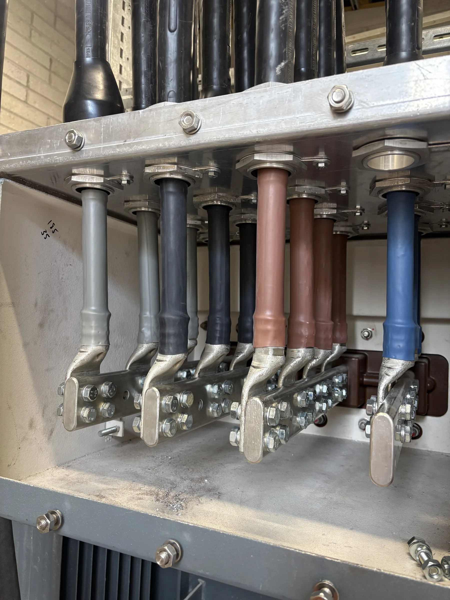 Grey, black, brown and blue insulated cables connected to metal terminals inside an open electrical cabinet.