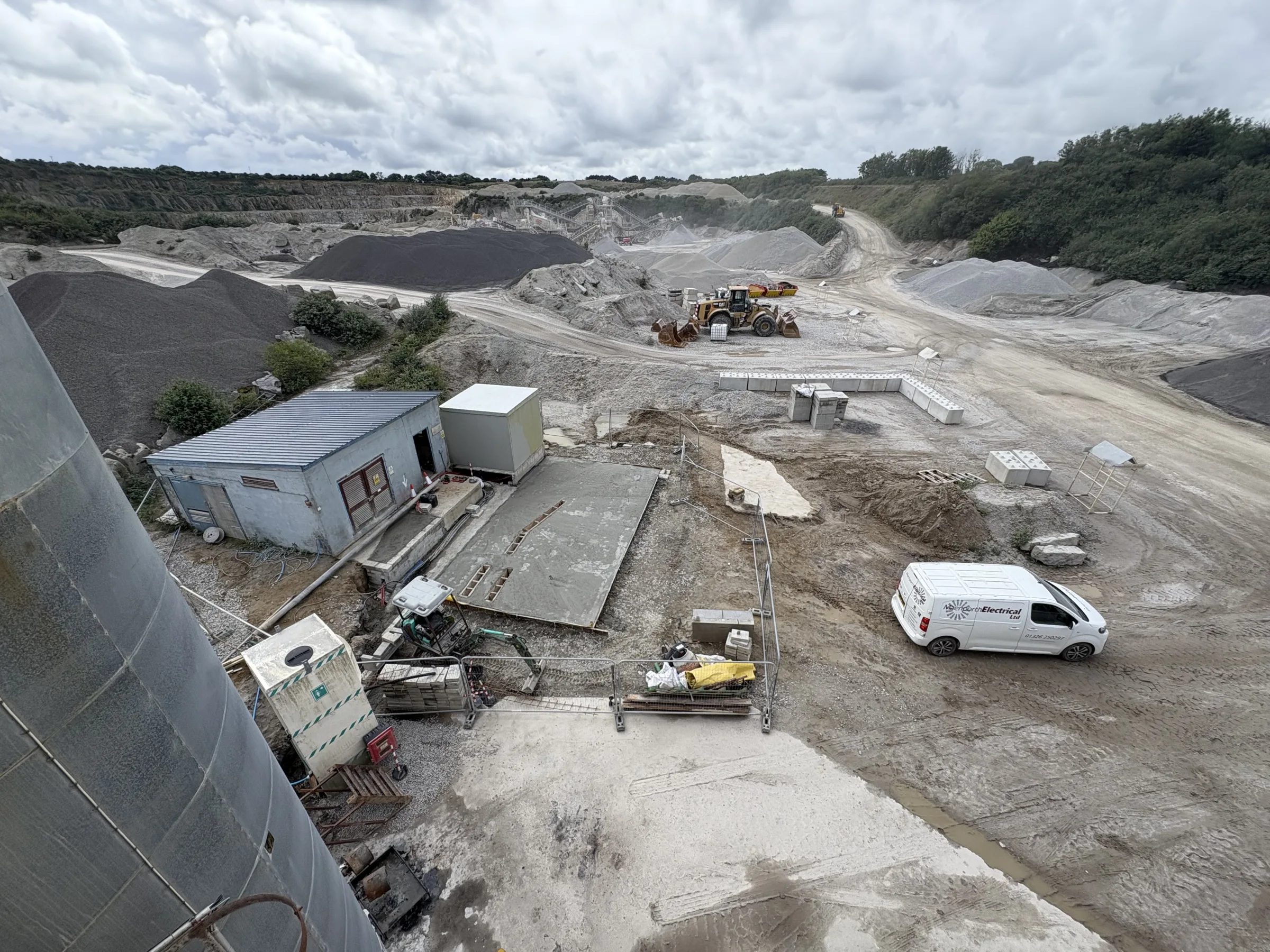 Elevated view across a quarry work area with aggregate piles, machinery, site buildings and a white van.