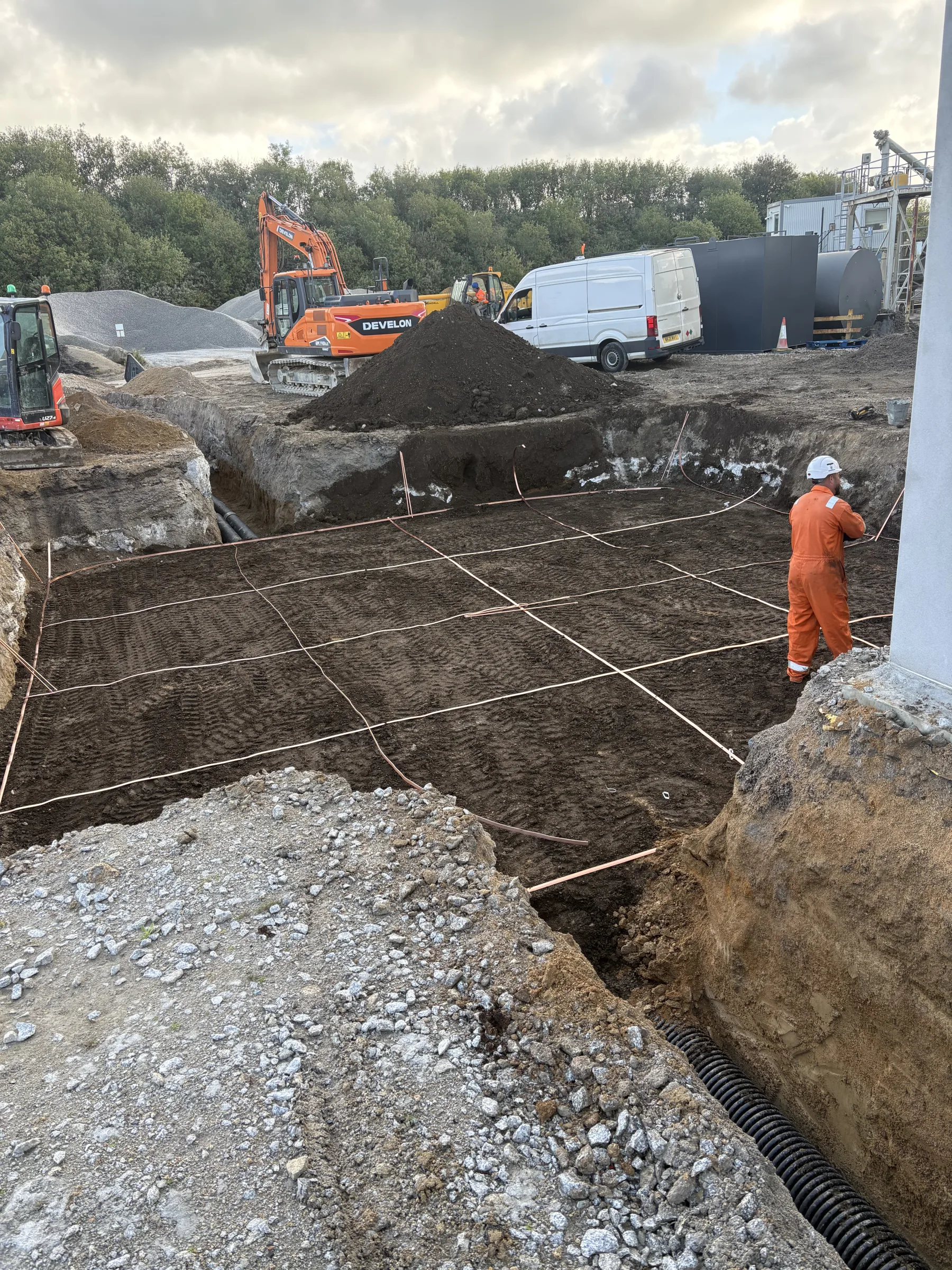 Grid of bare copper-coloured conductors laid across the base of a large excavation, with a worker, excavators and a white van nearby.