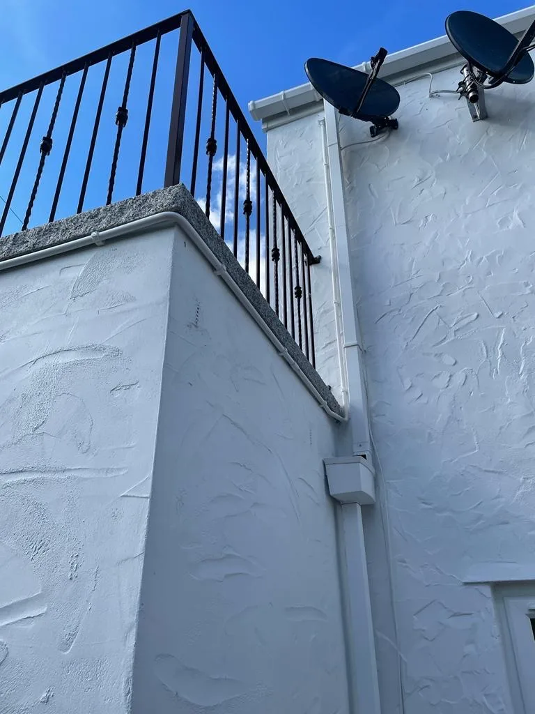 Vertical white cable casing running between two white rendered walls, with a small junction enclosure and two satellite dishes above.