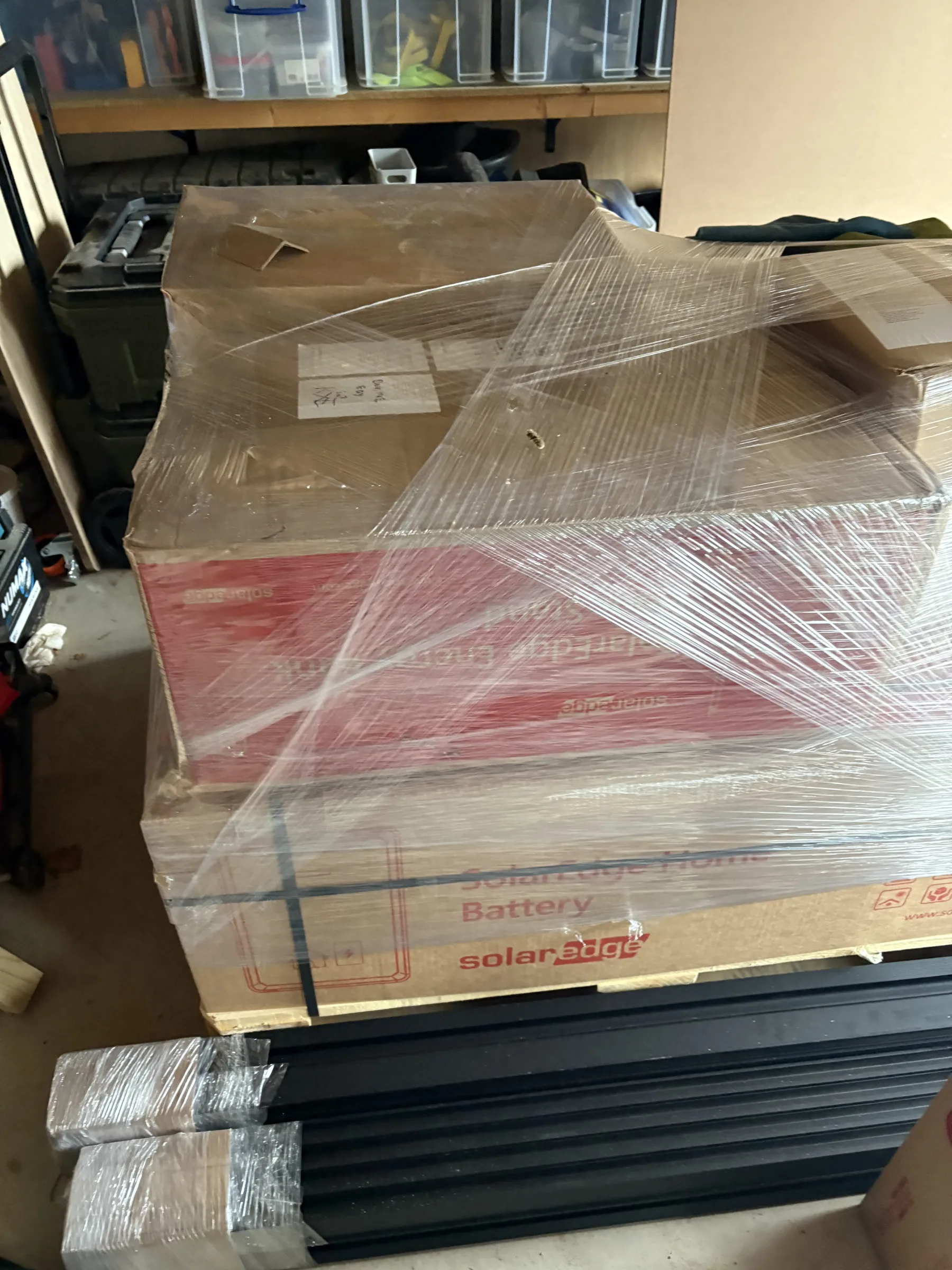 Large boxed battery equipment wrapped in clear plastic on a pallet, with bundled black metal mounting rails in front.