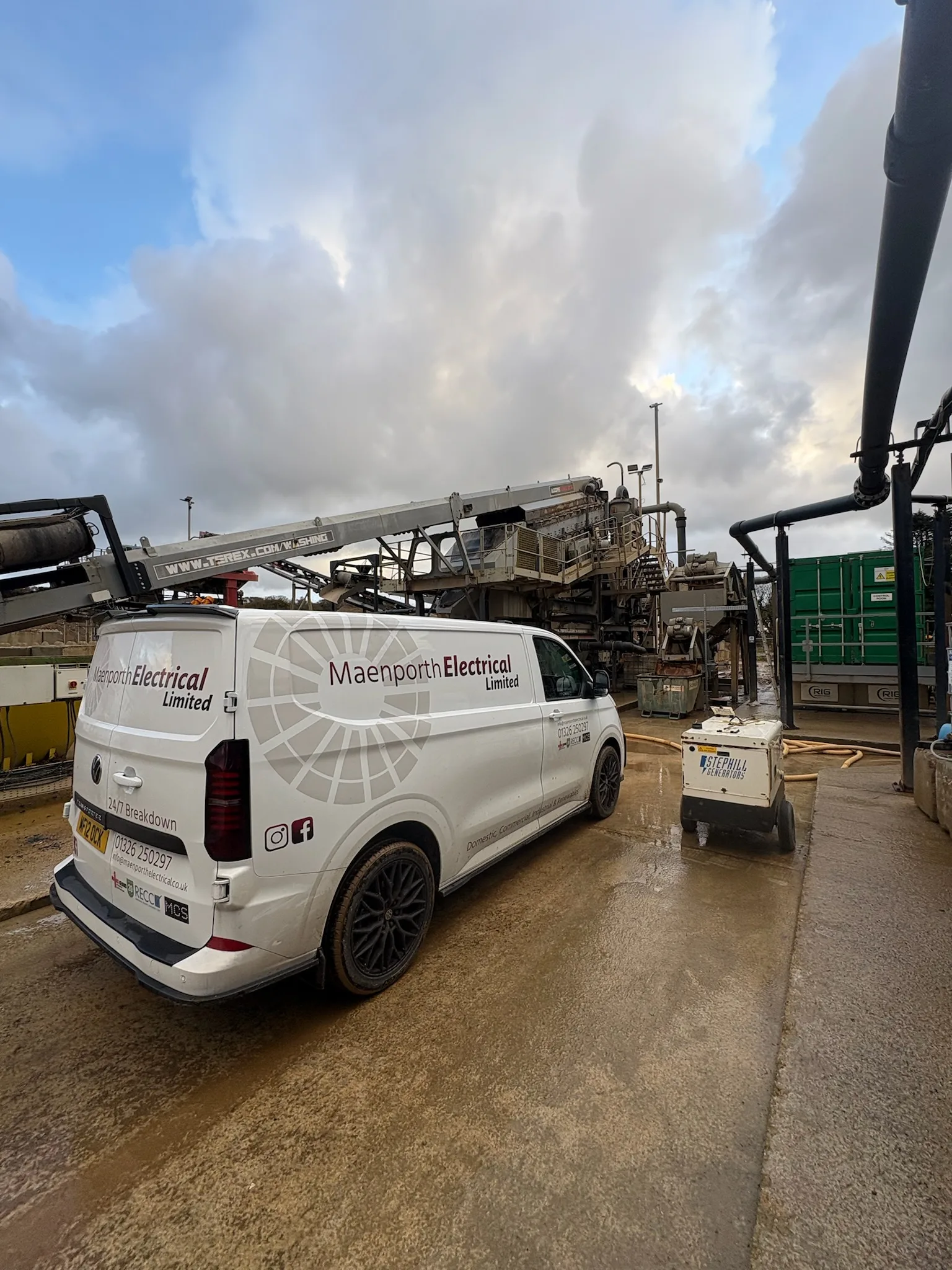 White Maenporth Electrical van parked on a wet industrial yard among conveyors, pipework, machinery and containers.
