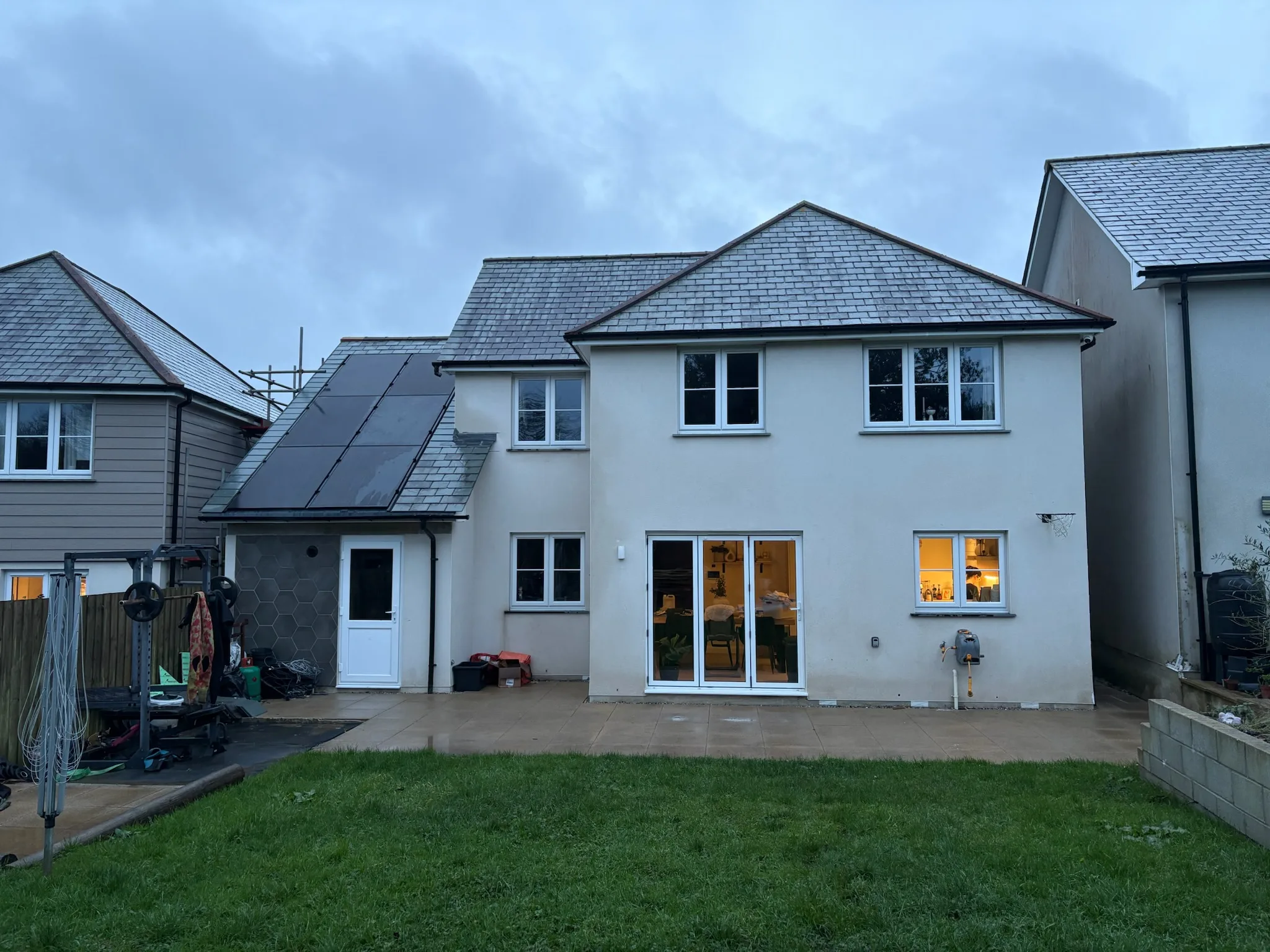 Rear of a two-storey rendered house with patio doors, several windows, a lawn and solar panels on the left-hand roof slope.